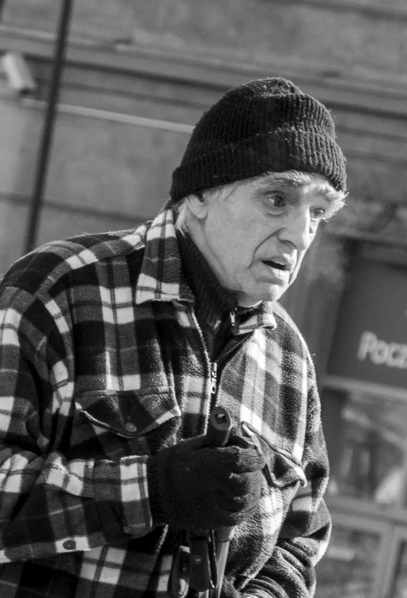 Older woman in a plaid jacket and knit cap gripping a cane with gloved hands